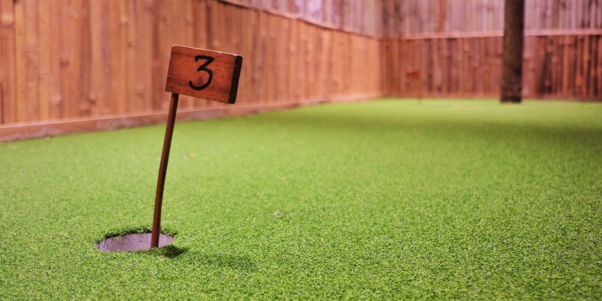 A number sign on the grass in front of a fence.